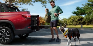 Homem sorridente com dois cachorros interagindo com a caçamba aberta da Chevrolet Montana na cor Vermelho Scarlet, em ambiente externo arborizado
