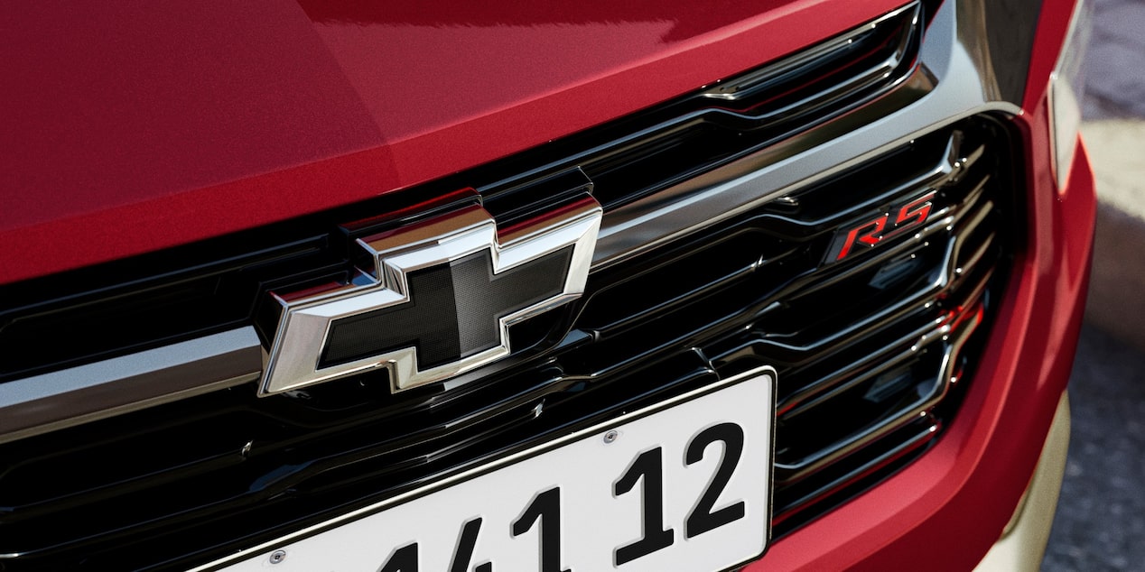 Close da grade frontal da Chevrolet Montana na cor Vermelho Scarlet com logotipo Chevrolet preto e emblema RS