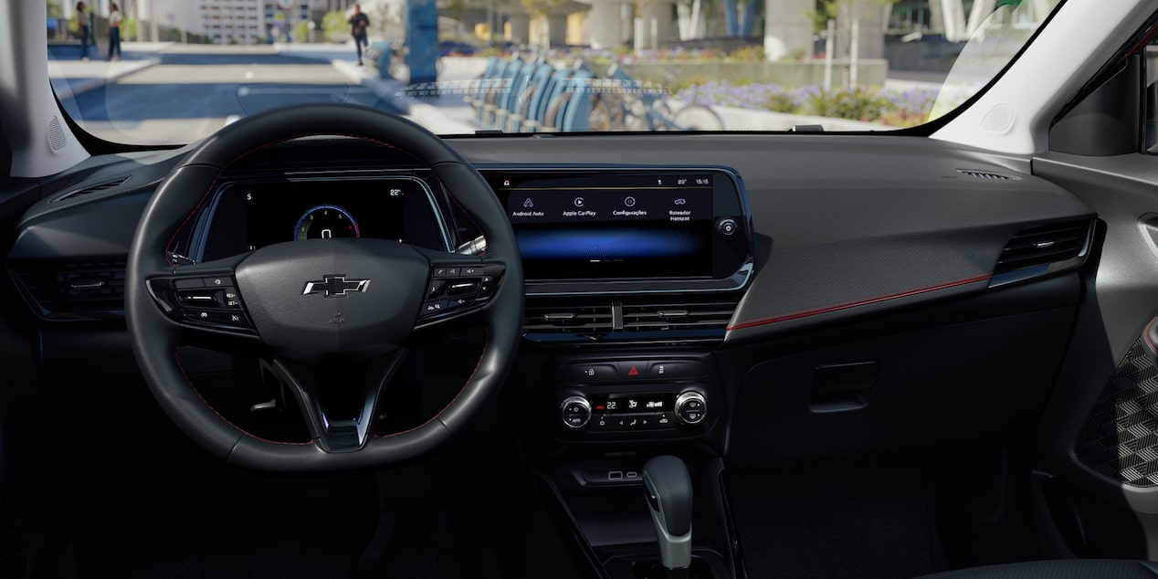 Volante e painel da Chevrolet Montana com acabamento escurecido e fundo de cidade urbana ao dia