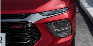 Close do conjunto óptico dianteiro da Chevrolet Montana na cor Vermelho Scarlet com farol de LED e emblema RS em fundo urbano
