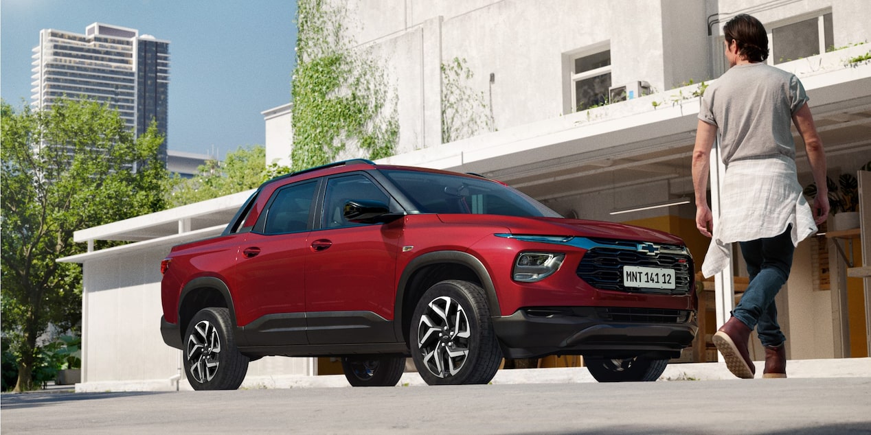 Chevrolet Montana na cor Vermelho Scarlet estacionada em frente a prédio urbano moderno com homem caminhando ao fundo