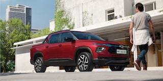 Chevrolet Montana na cor Vermelho Scarlet estacionada em frente a prédio urbano moderno com homem caminhando ao fundo
