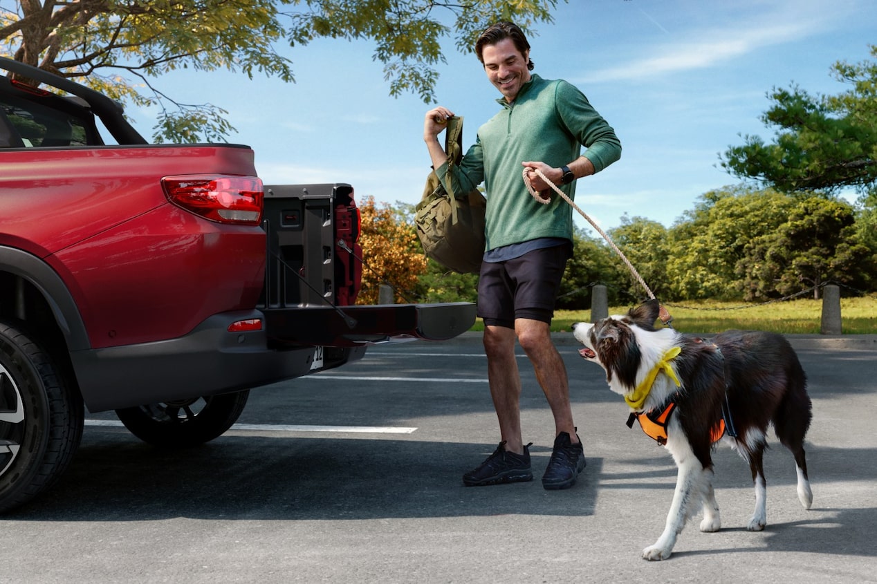 Homem sorridente com dois cachorros interagindo com a caçamba aberta da Chevrolet Montana na cor Vermelho Scarlet, em ambiente externo arborizado
