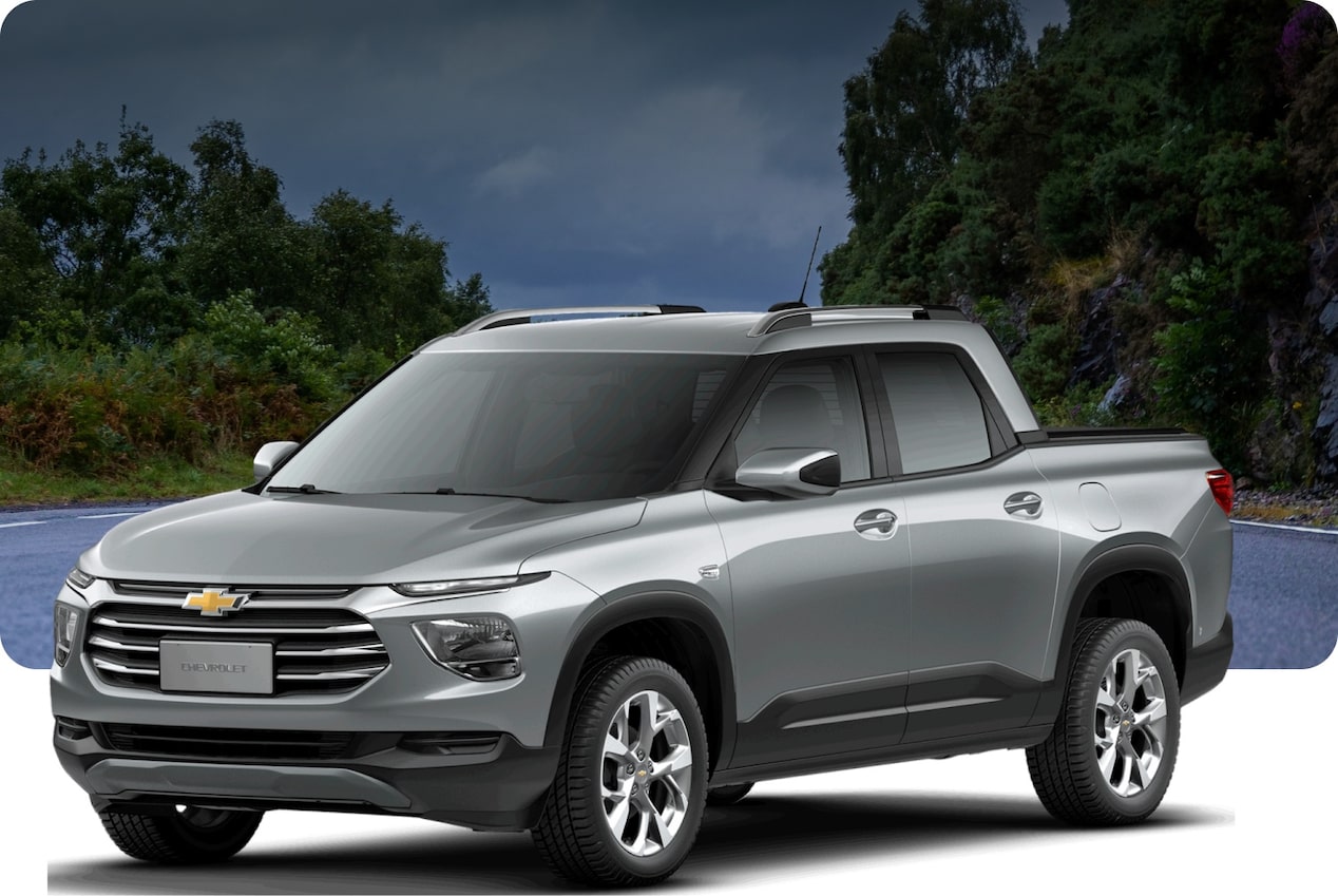 Chevrolet Montana prata estacionada em frente a uma paisagem com vegetação e lago ao entardecer