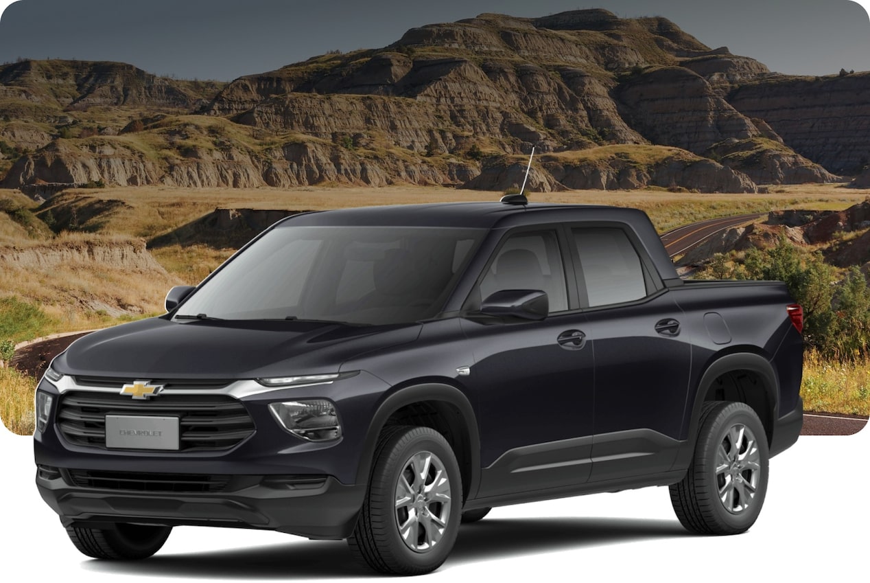 Chevrolet Montana cinza em estrada de terra com montanhas rochosas ao fundo