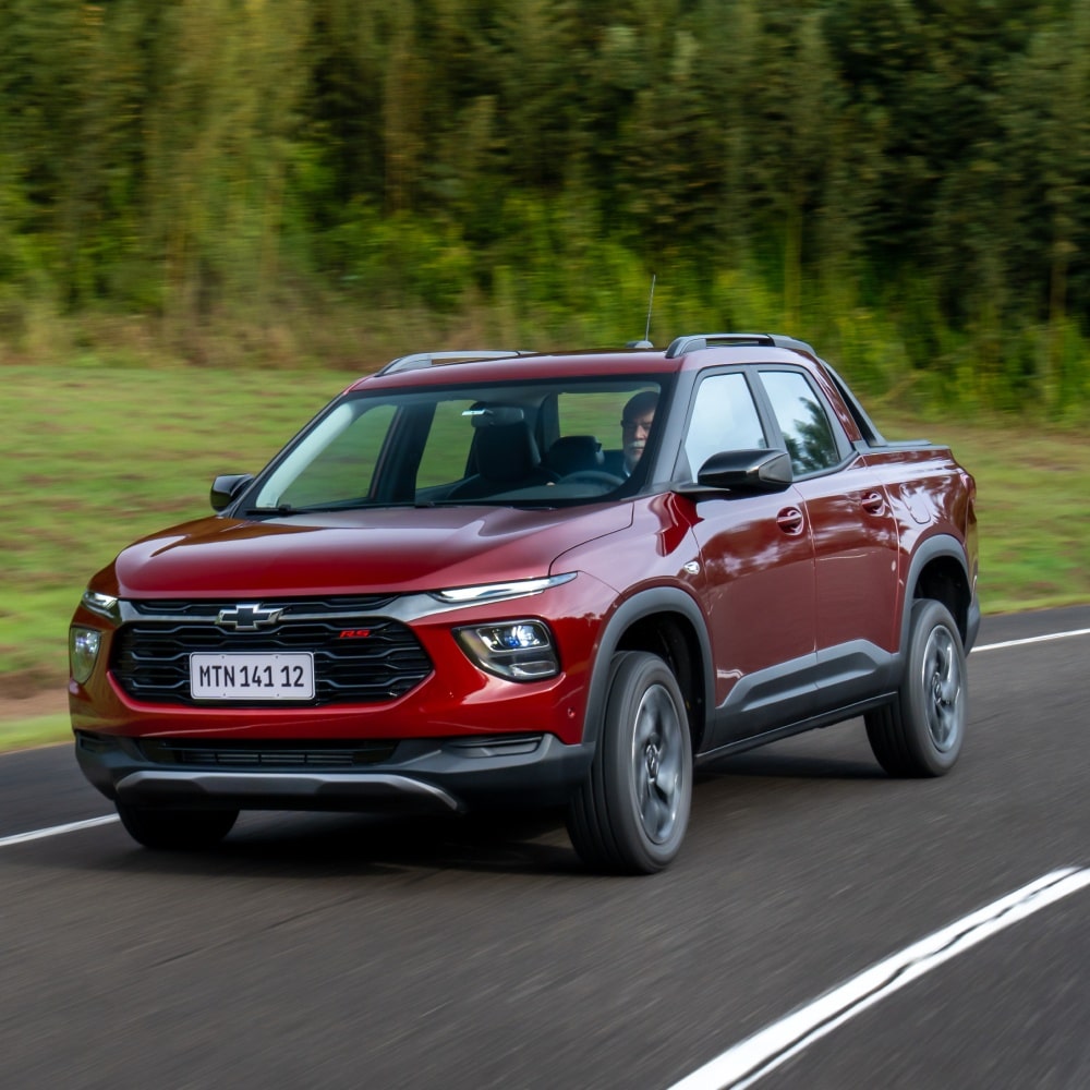 Chevrolet Montana vermelha em movimento na estrada, com vegetação ao fundo. Á direita, o carro; a esquerda, o texto: Montana 2027 – a partir de R$ 00.000 ou com entrada de R$ 00.000 e 00 parcelas de R$ 000 e os botões explorar ofertas e encontre seu Chevrolet.