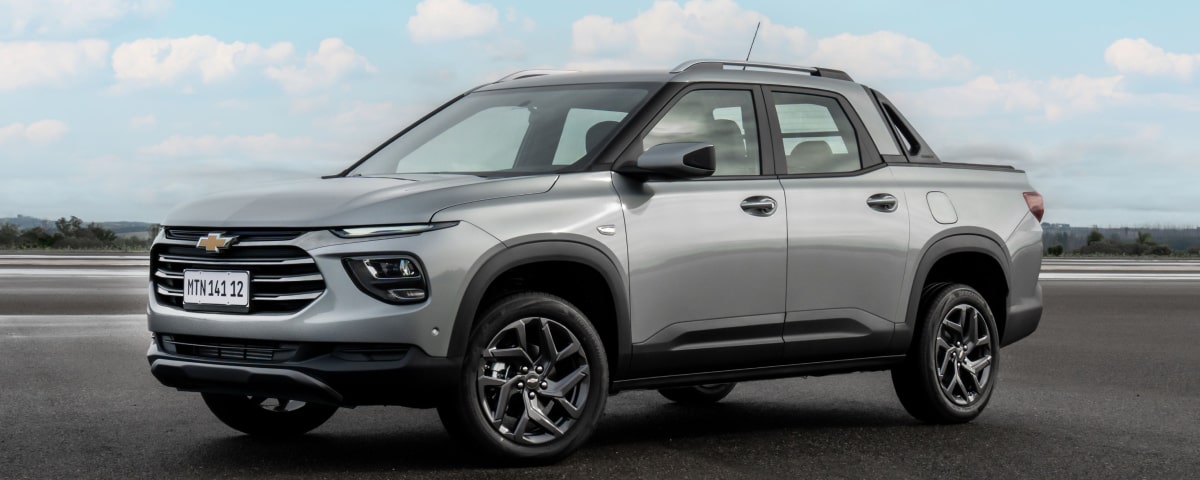 Chevrolet Montana estacionada em um espaço aberto. Vemos todo o carro em destaque no centro da imgaem. Ao fundo, um céu azul e ensolarado.