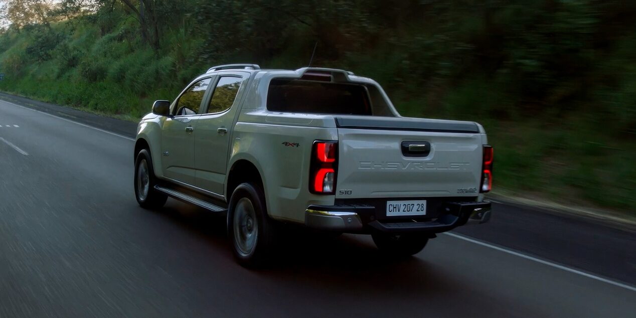 Chevrolet S10 andando na estrada, com destaque para sua lateral e traseira. Ao fundo, uma paisagem com bastante vegetação.