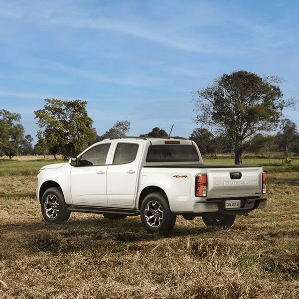 Chevrolet S10 High Country estacionada em um ambiente aberto, fora da estrada. Ao fundo, um grande campo aberto com árvores, indicando o estilo off road do modelo.​