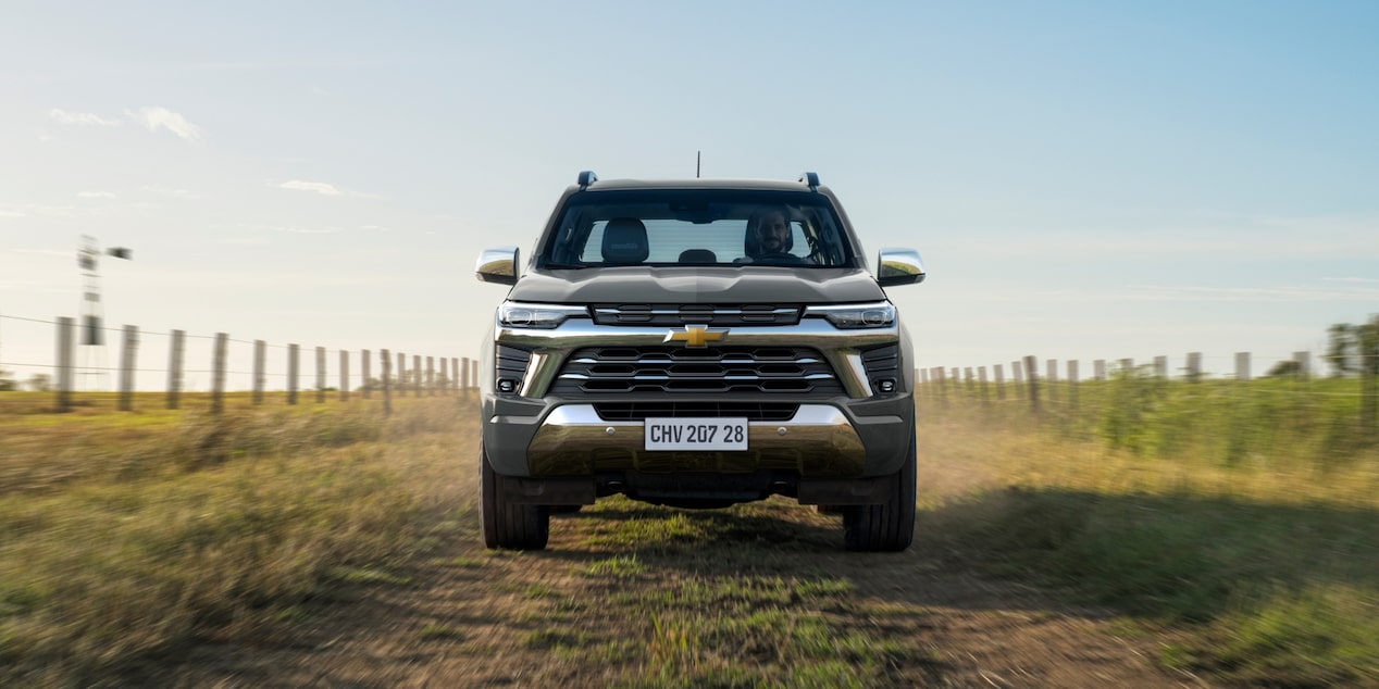 Chevrolet S10 vista de frente, em movimento por uma estrada de terra cercada por vegetação e cercas.