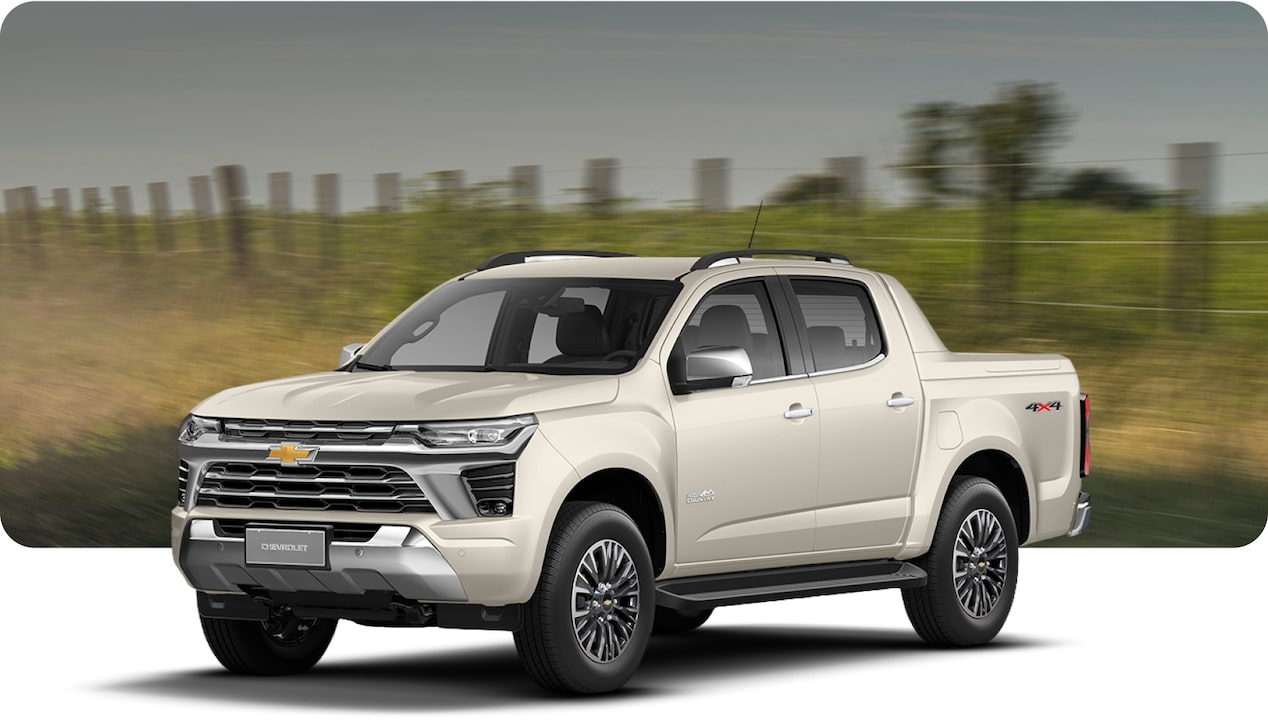 Chevrolet S10 High Country em perspectiva. Vemos a lateral esquerda e toda parte frontal do modelo. Ao fundo uma paisagem rural com cercas e plantas.