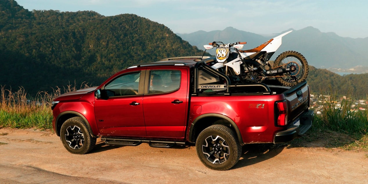 Chevrolet S10 Z71 vermelha vista de perfil, com motocicleta na caçamba, rodas com acabamento escurecido e emblema Z71.