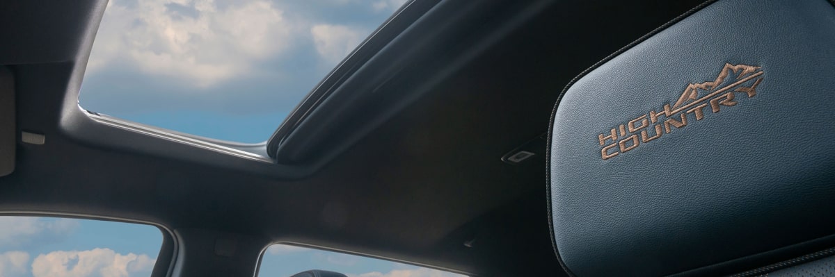 Detalhe do logo High Country no banco do motorista encimado pelo teto solar panorâmico da Chevrolet Silverado a para a página de acessórios originais da respectiva picape.