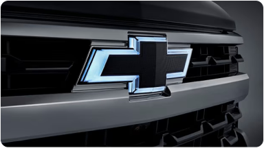 Imagem em close da grade dianteira da nova picape Chevrolet Silverado, preto, dando destaque ao logo Chevrolet iluminado; com neon em sua volta.