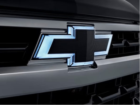 Imagem em close da grade dianteira da nova picape Chevrolet Silverado, preto, dando destaque ao logo Chevrolet \"iluminado\" com neon em sua volta.