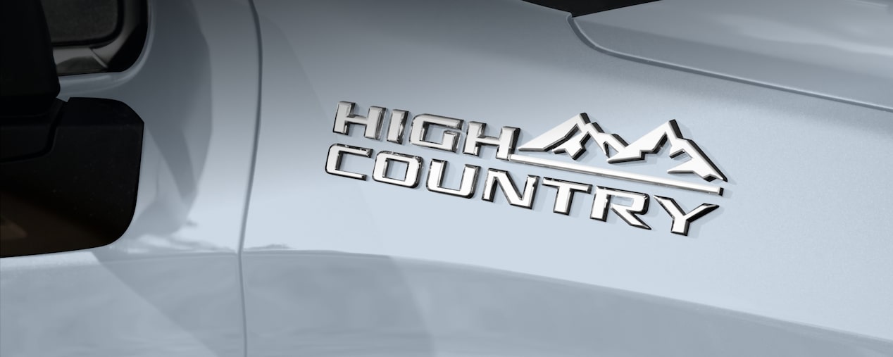 Mastehead da página de Acessórios universais dos acessórios originais Chevrolet para a picape Silverado, com foco no badge da versão High Country disposto na porta do motorista.