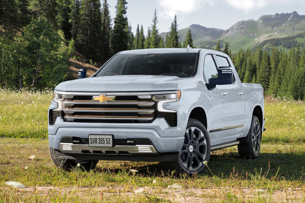 Imagem de uma Chevrolet Silverado na cor branca sob a grama com montanhas ao fundo.