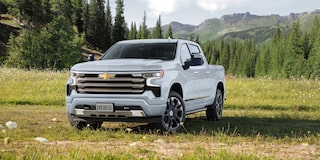 Imagem de uma Chevrolet Silverado na cor branca sob a grama com montanhas ao fundo.