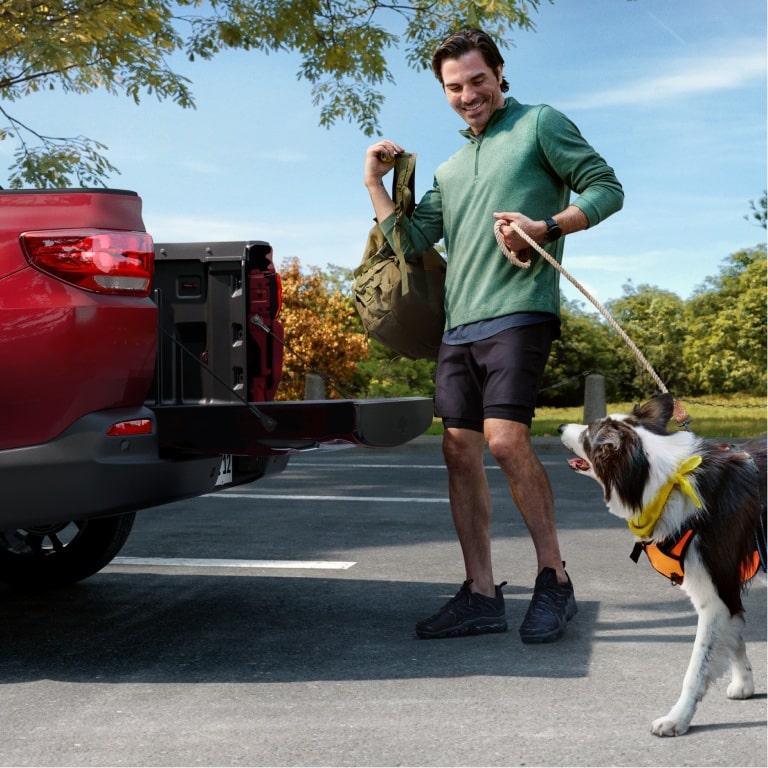 Homem embarcando cãozinho na caçamba de uma picape Chevrolet.