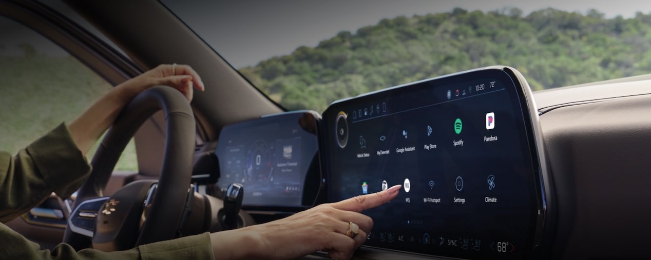 Banner principal da página da central multimídia MyLink. Na imagem, uma motorista toca na tela da central enquando dirige seu Chevrolet. No quadrante superior esquerdo, o texto: Chevrolet MyLink - Você conectado em todos os momentos.