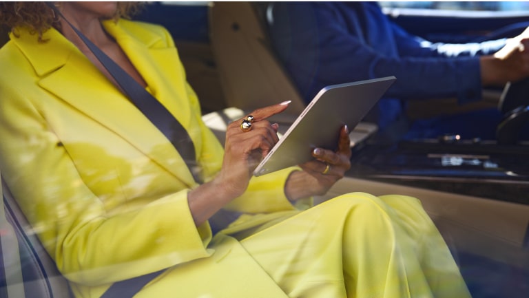 Pessoa sentada dentro do carro, vestindo roupa amarela, utilizando um tablet enquanto o veículo está parado.