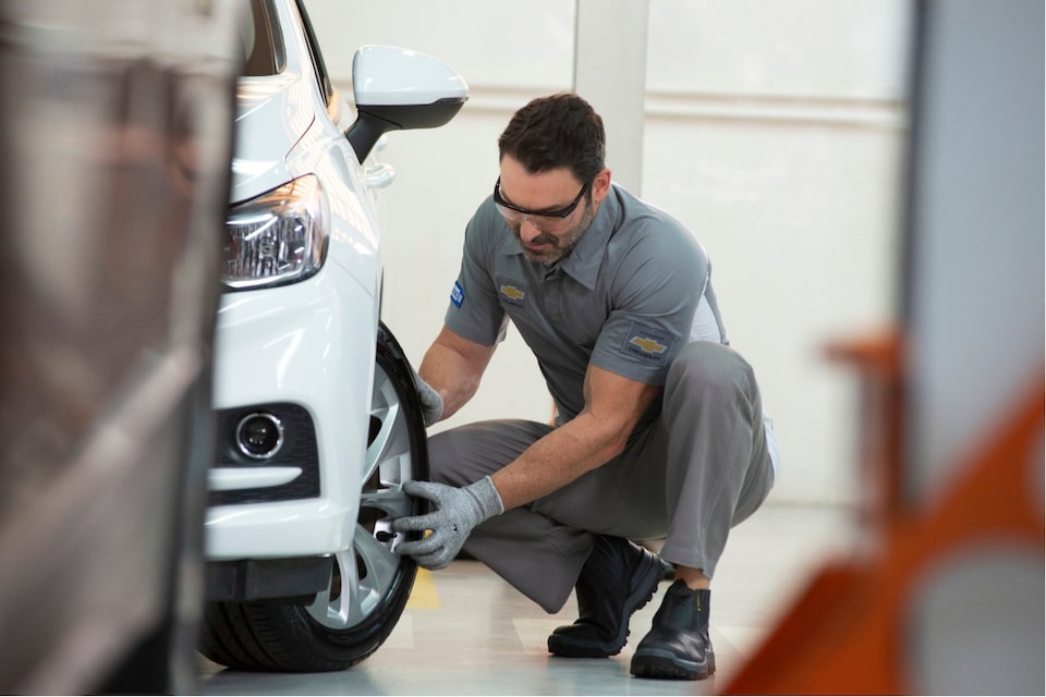 Mecânico trabalha na roda dianteira de um Chevrolet Branco.