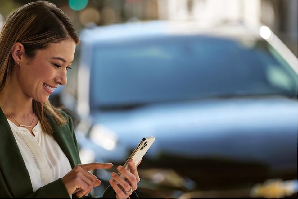 No primeiro plano, uma mulher mexe no celular, navegando no app myChevrolet. No segundo plano, um Chevrolet.