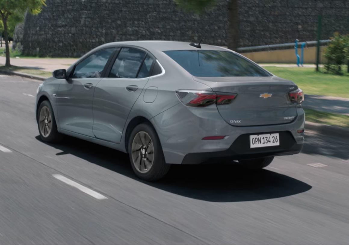 um Onix Plus Prata andando em uma rodovia. Vemos a traseira e lateral do veículo.