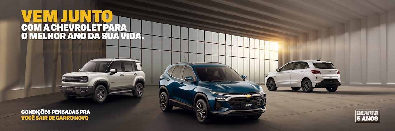 Banner predominantemente escuro, com um Spark EUV, Tracker e um Onix, dispostos em ordenação triangular diante de uma grande janela por onde entra a luz que alumia a cena. No quadrante superior esquerdo, o texto: Vem junto com a Chevrolet para o melhor ano da sua vida. No quadrante inferior esquerdo, com um texto condições pensadas pra você sair de carro novo. No quadrante inferior direito, o selo de 5 anos de garantia Chevrolet.
