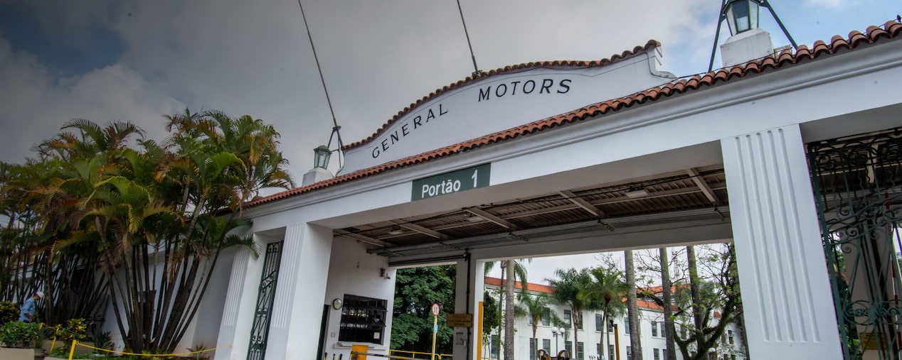 Entrada principal da fábrica da General Motors em São Caetano do Sul, com portão branco identificado como Portão 1 e letreiro General Motors no topo.