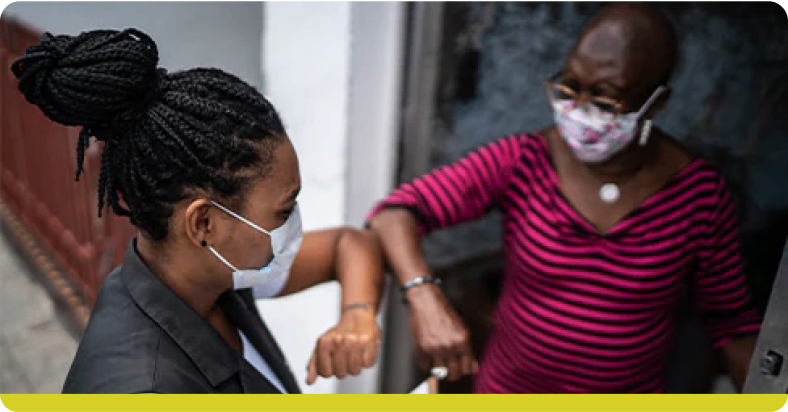 Duas senhoras de máscara de proteção respiratória se cumprimentando com os cotovelos