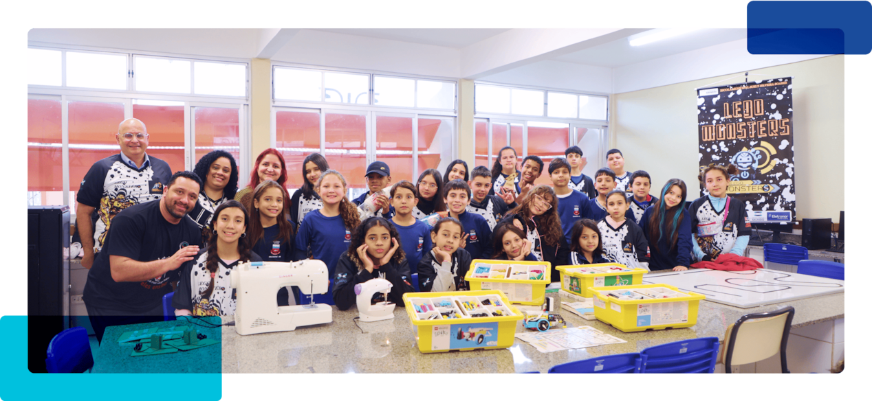 Professores e crianças em uma sala de aula com máquinas de costura sob uma bancada