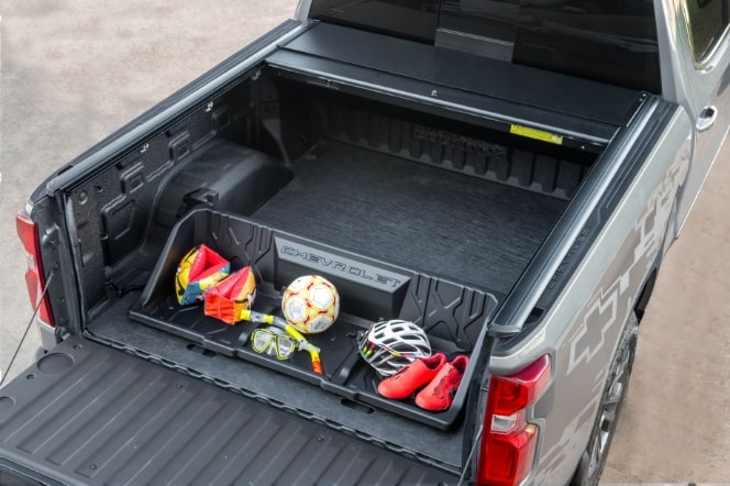 Imagem mostrando caçamba da nova picape Chevrolet Silverado, destacando o acessório "bolsa dupla". Na bolsa, brinquedos, bola, sapato esportivo e capacete de bicicleta.